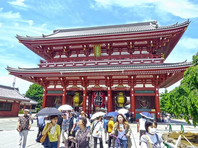 Large multi-tiered red temple gate overlooking a bustling sunny plaza filled with tourists