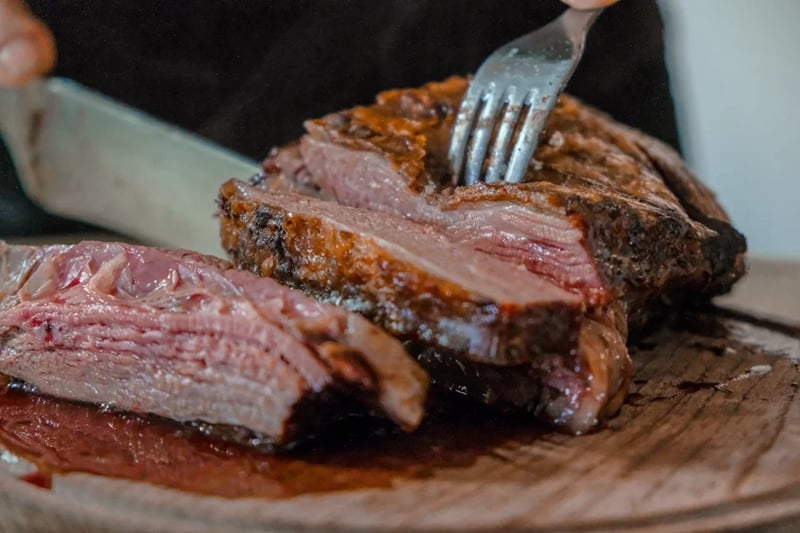 Person holding fork with meat, plate of meat behind
